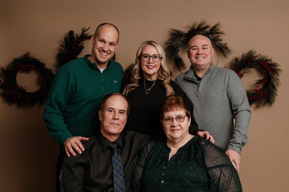 Studio portrait showing a group of five people in casual dress against a tan background with holiday wreaths on the wall.
