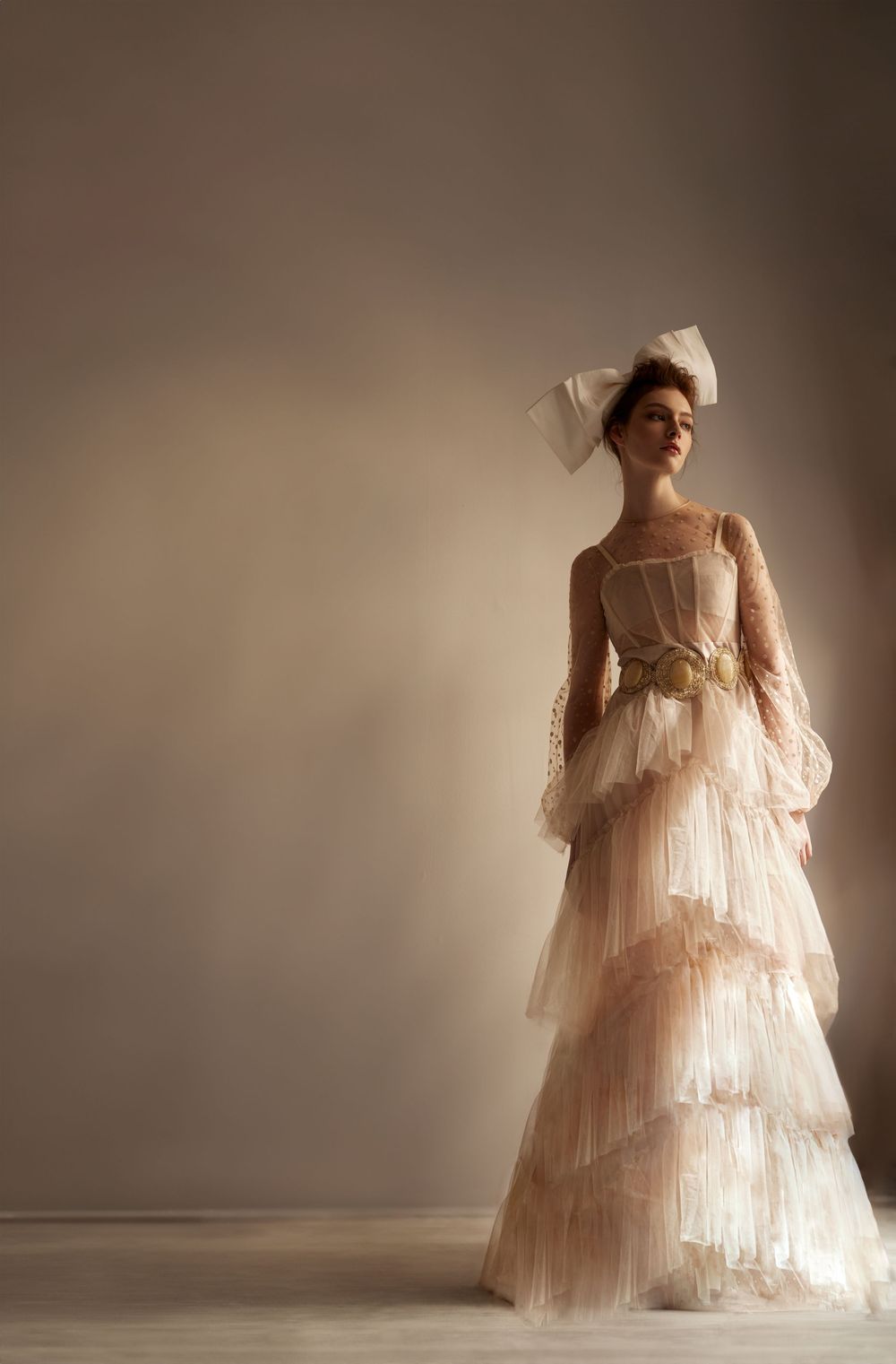 A stunning vintage-inspired wedding gown with tiered ruffles and delicate lace details stands elegantly in soft lighting.
