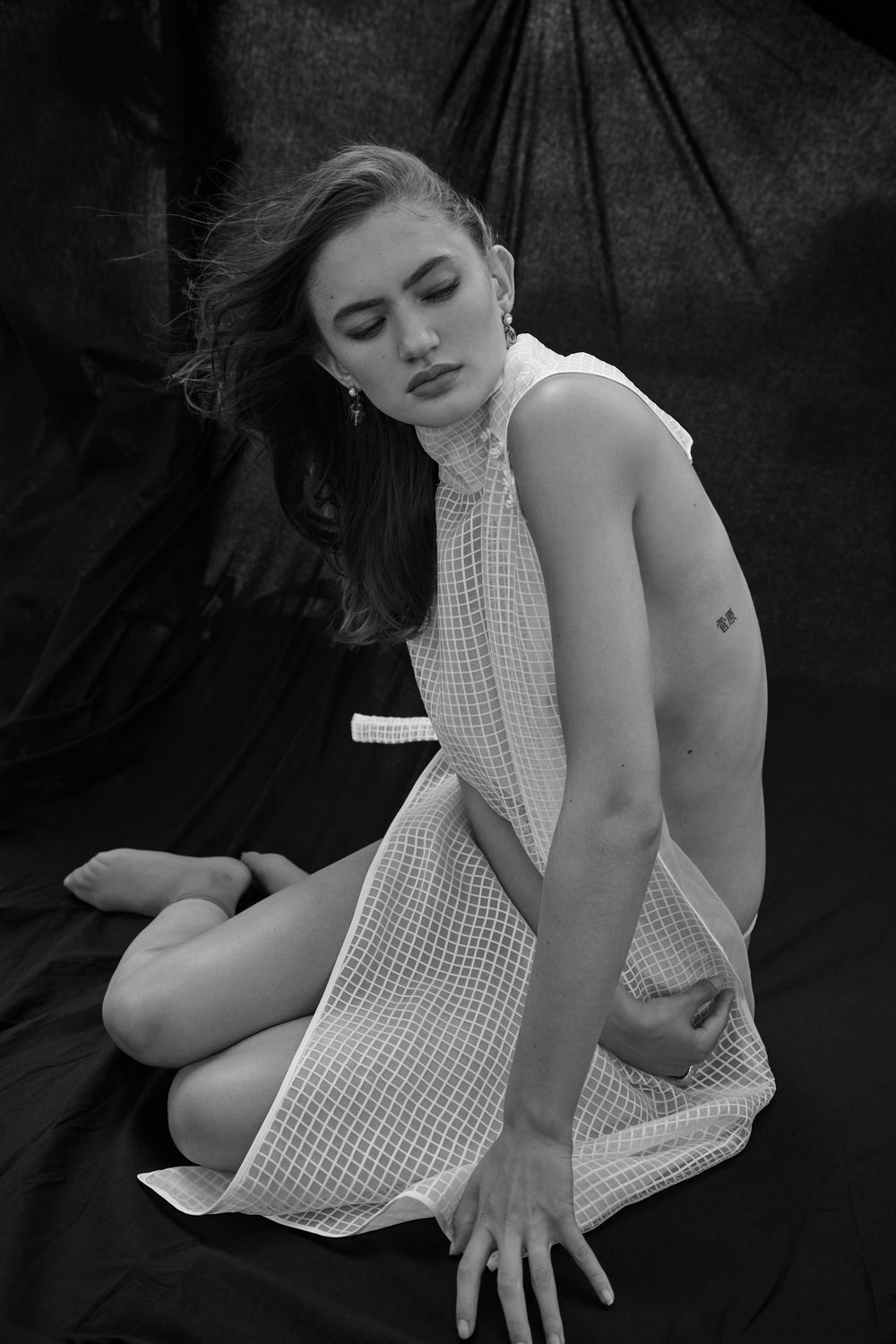 Black and white artistic photograph showing graceful pose in checkered halter dress against dark background.