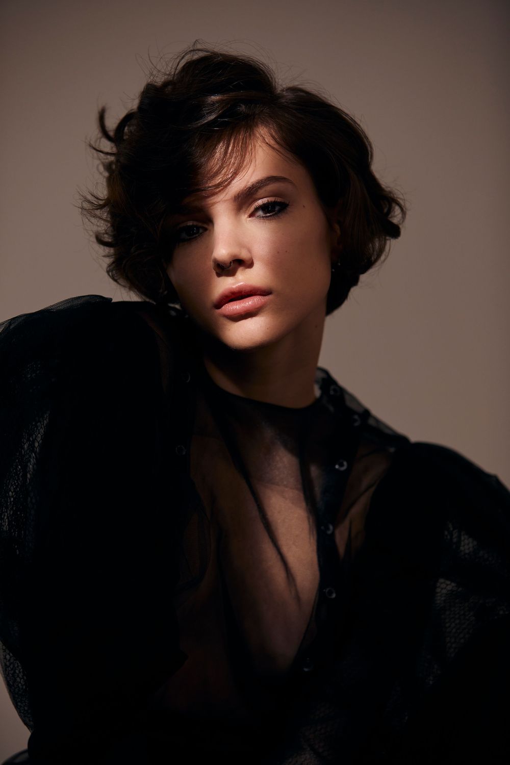 Dramatic portrait featuring short dark tousled hair and black sheer clothing against moody lighting.