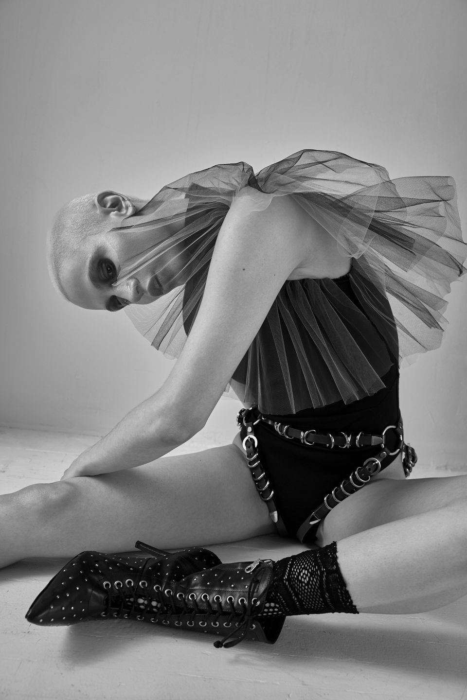 Artistic black and white photo showing a dancer in a tutu skirt and studded boots bending forward in a dramatic pose.