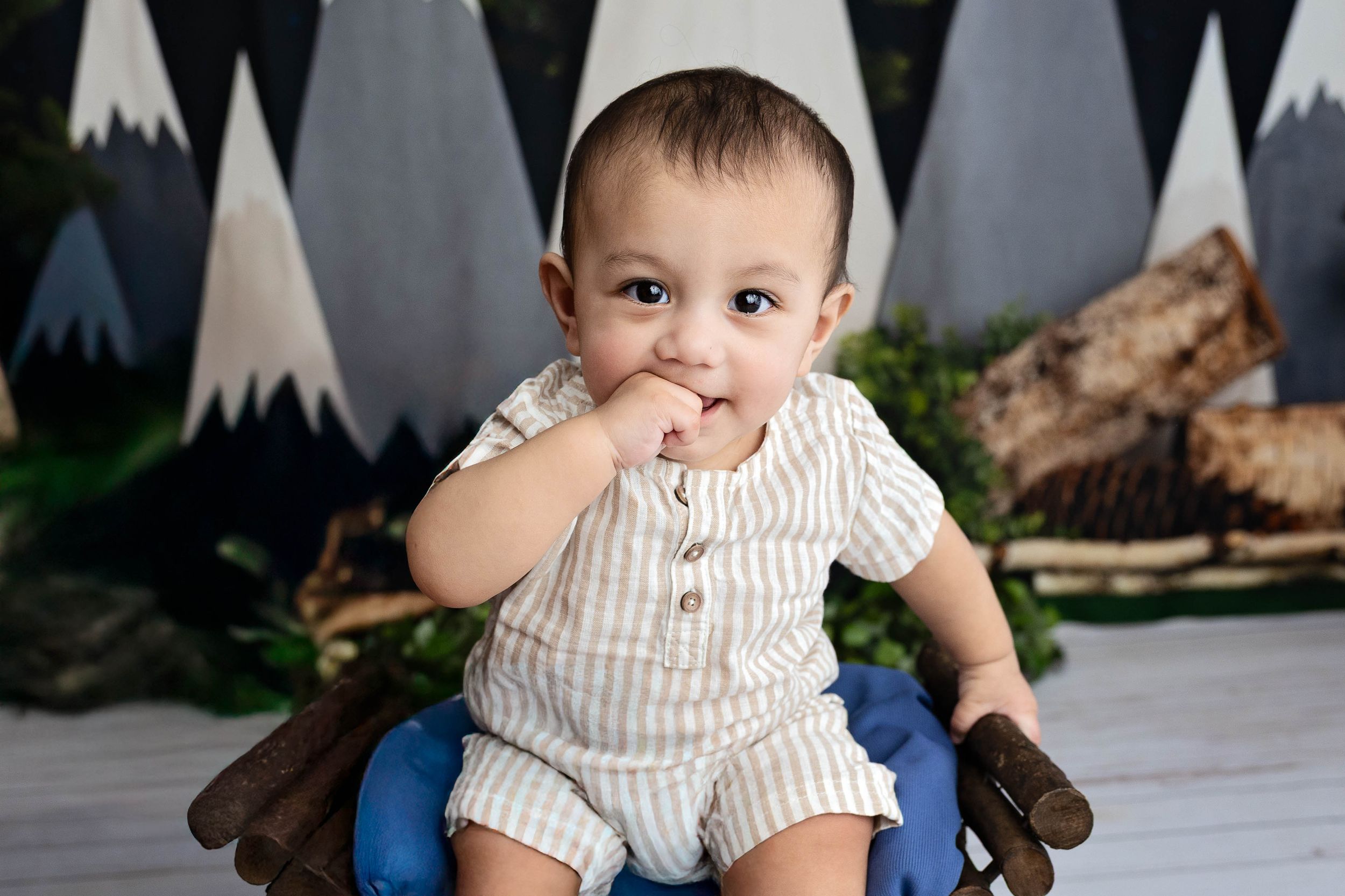 Baby in striped romper sits on blue cushion against mountain-themed backdrop. #6monthpictures #Photographer #CarlsbadNM #ArtesiaNM #Roswell