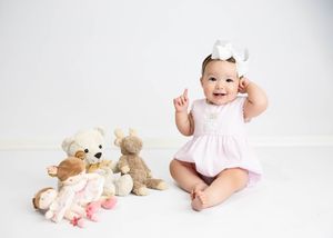 Smiling baby in pink dress sits on white backdrop with plush teddy bears beside them. #RoswellNM #CarlsbadNM #firstyearphotos #kidphotograph