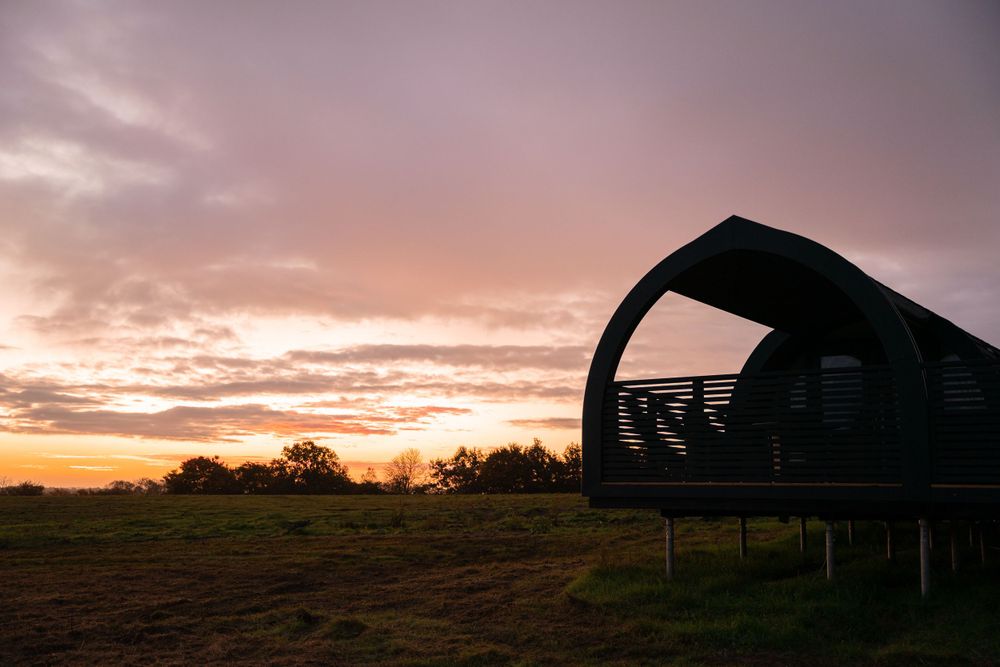 Modern cabin with curved black roof silhouetted against a dramatic orange and purple sunset sky. Lincolnshire branding photographer.