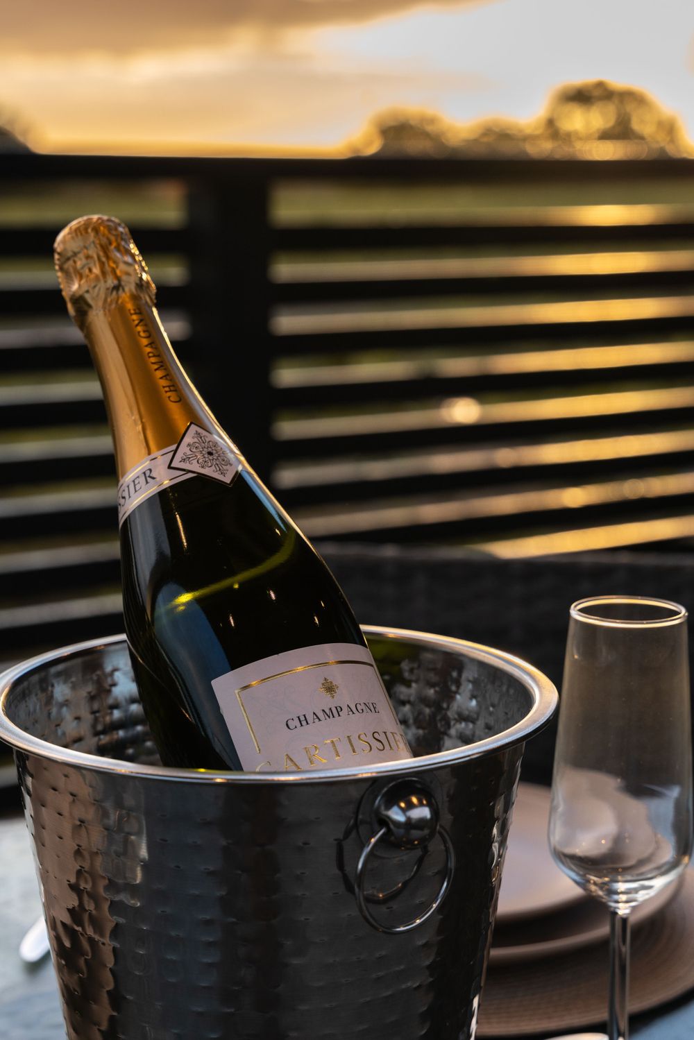 Champagne bottle chills in an ice bucket against a warm sunset background. Lincolnshire branding photographer.