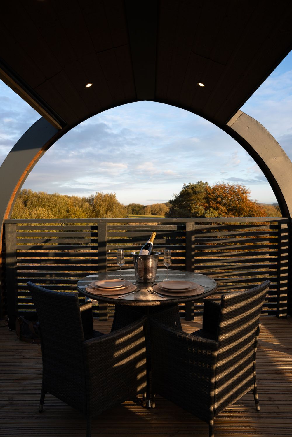 Cozy outdoor dining setup framed by an arch with horizontal slats overlooking autumn trees. Lincolnshire branding photographer.