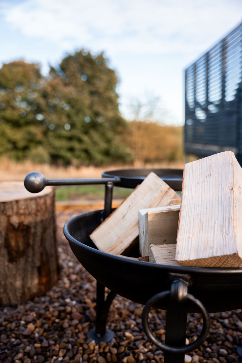 Fire pit filled with wooden logs on gravel ground with black metal frame. Lincolnshire branding photographer.