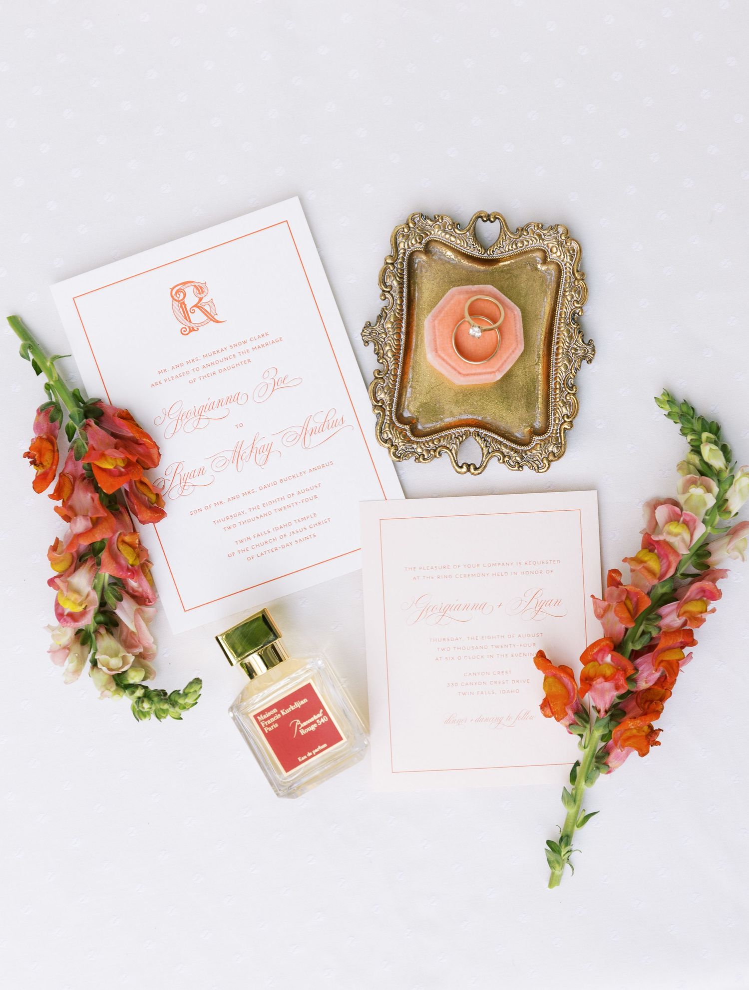 An elegant wedding invitation suite with coral flowers, perfume bottle and ornate gold frame on white background.