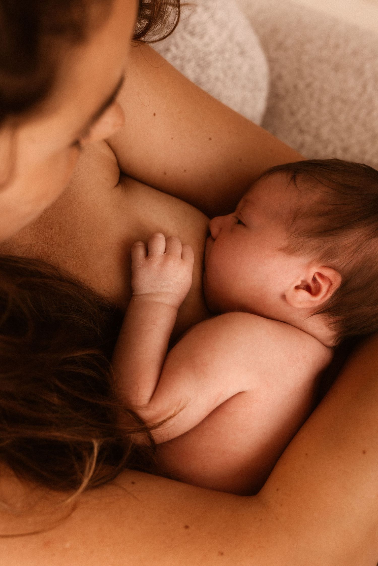 A tender moment of breastfeeding shows a tiny baby's hand resting against skin in warm, intimate lighting. Javea photographer