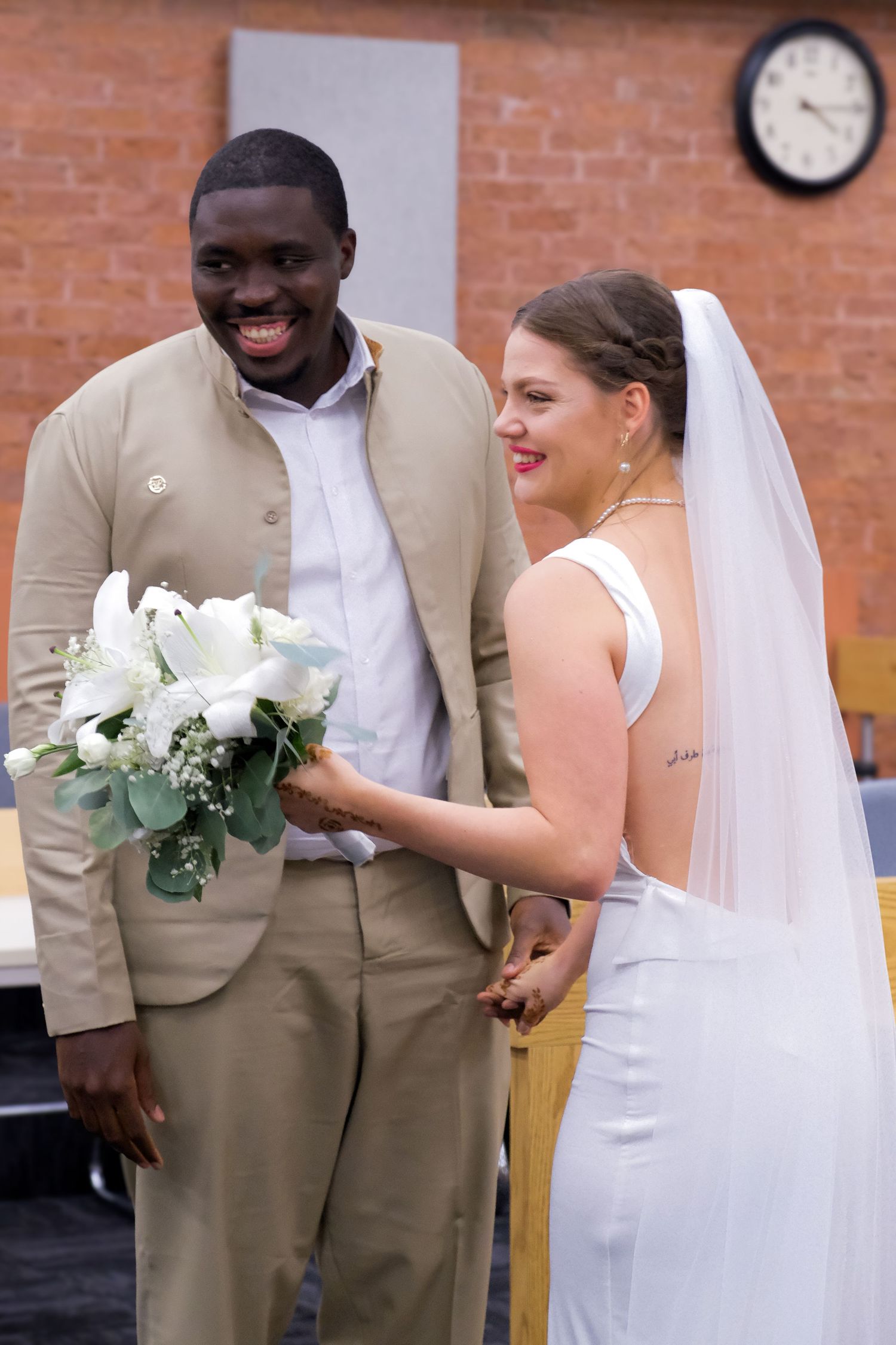 Wedding couple in white dress and tan suit sharing joyful moment during ceremony.