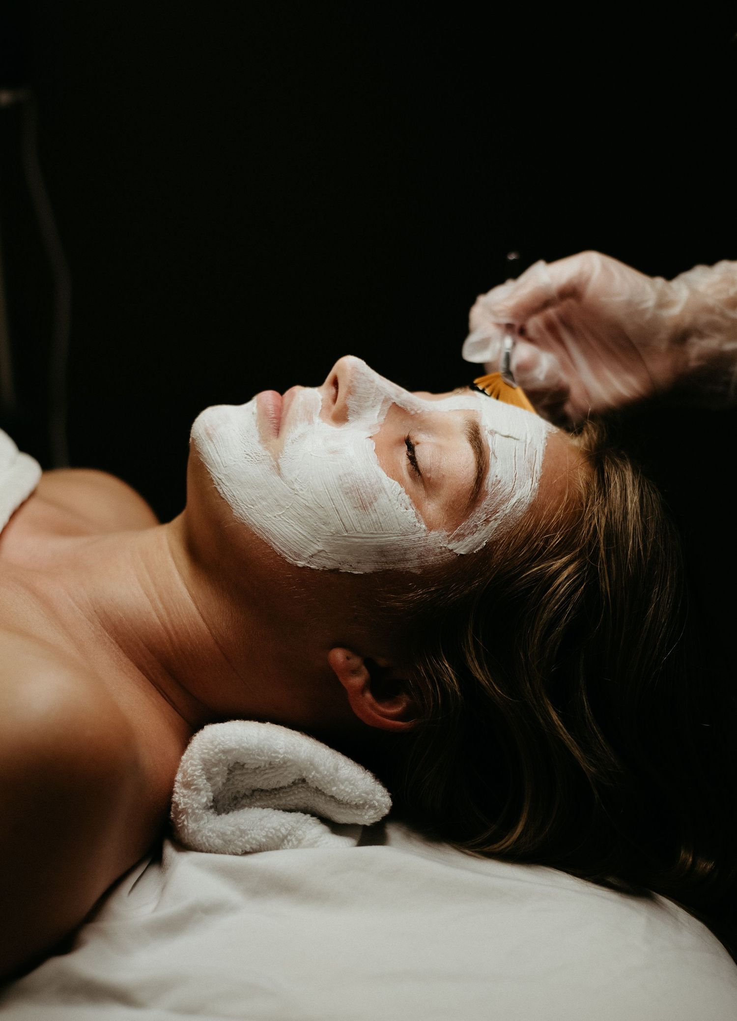 Artistic beauty photography showing facial mask treatment in dramatic lighting.