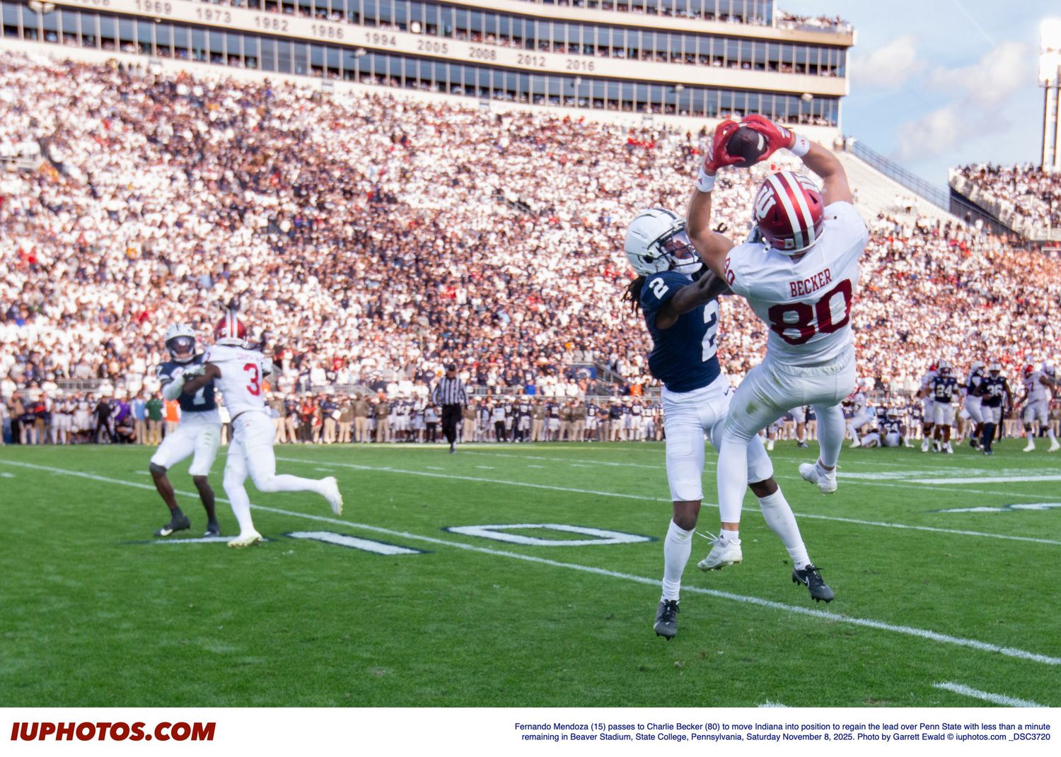 College football player leaps high to catch a pass during a game in a packed stadium.