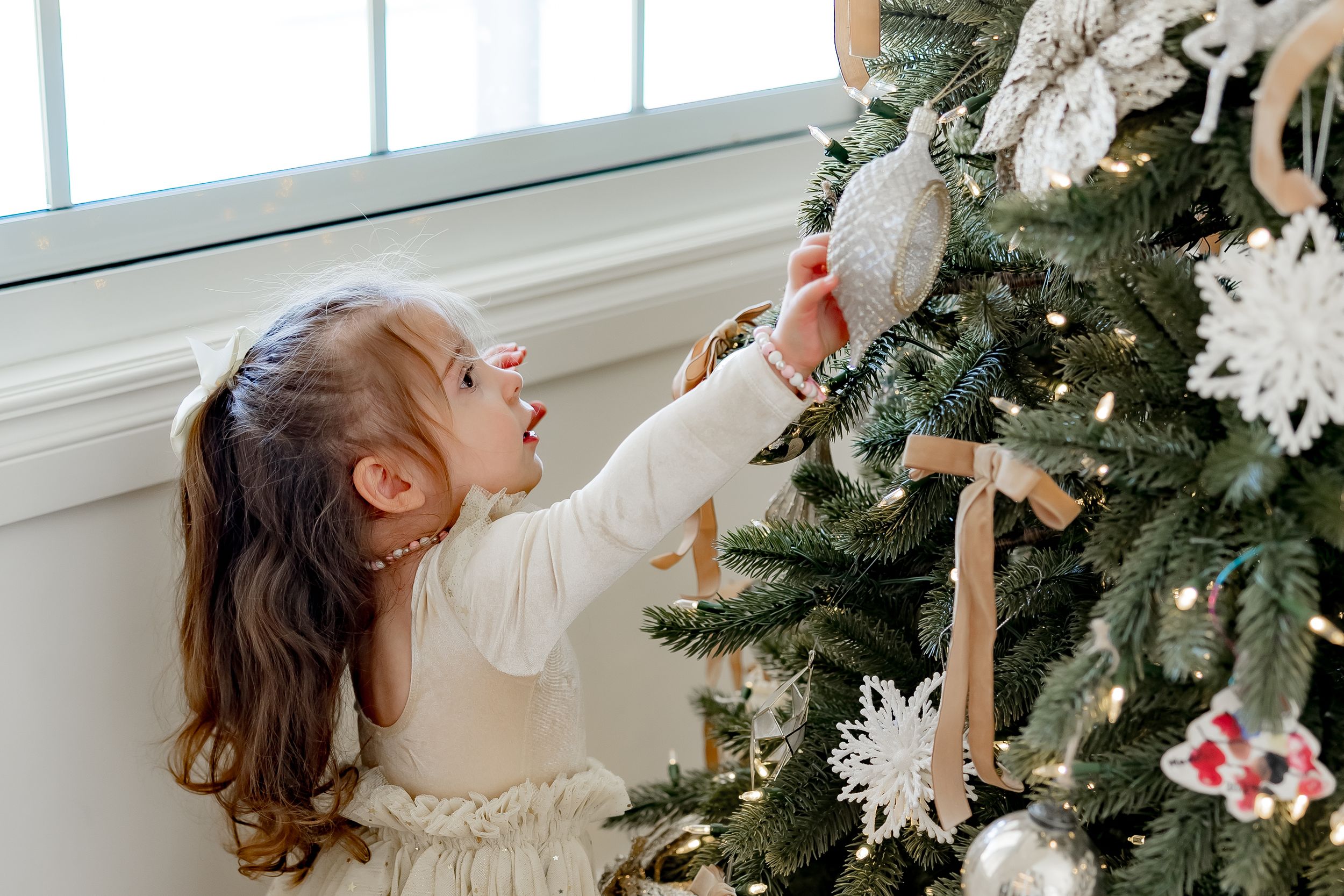 Holiday decor scene showing evergreen branches and white snowflake ornaments near a bright window.