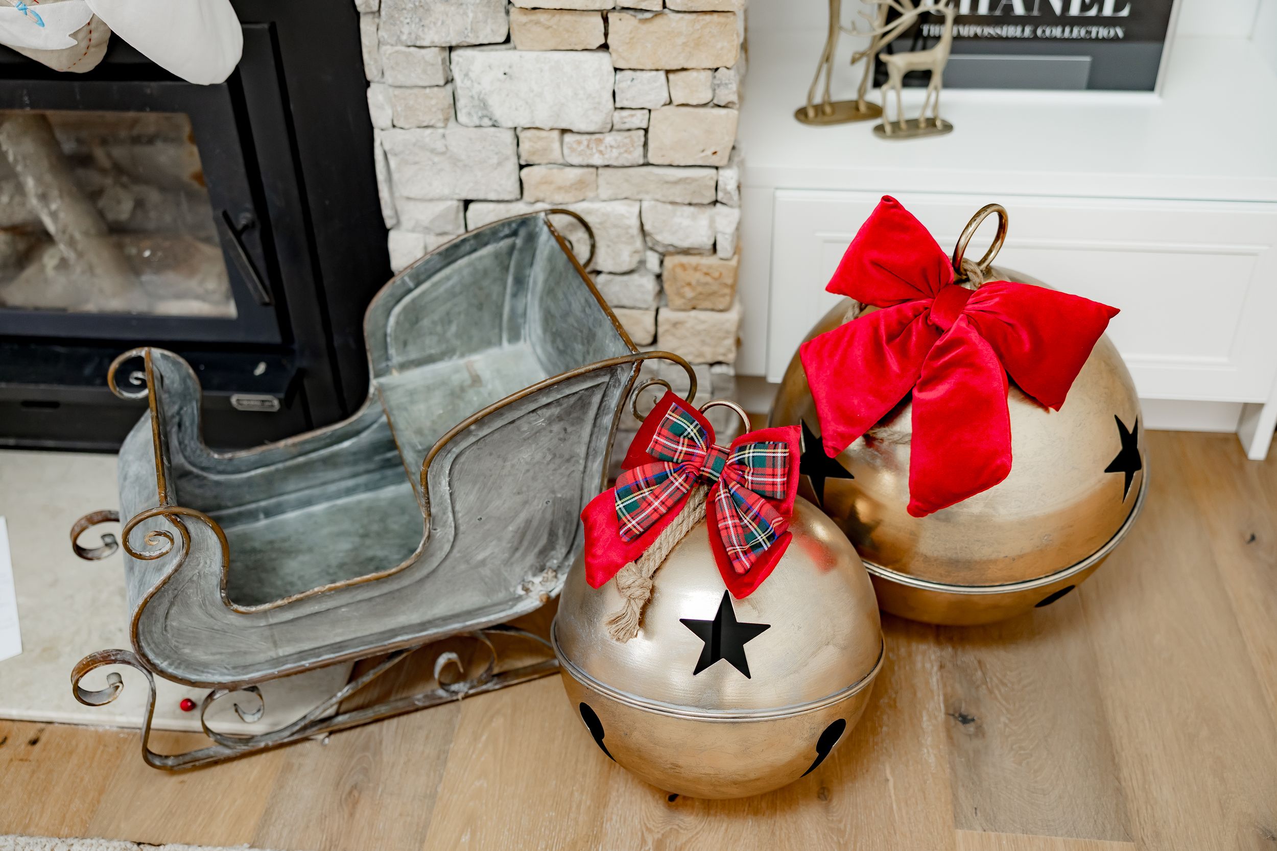 Rustic holiday decor featuring antique sleigh bells with red bows displayed on a white mantel against stone wall.
