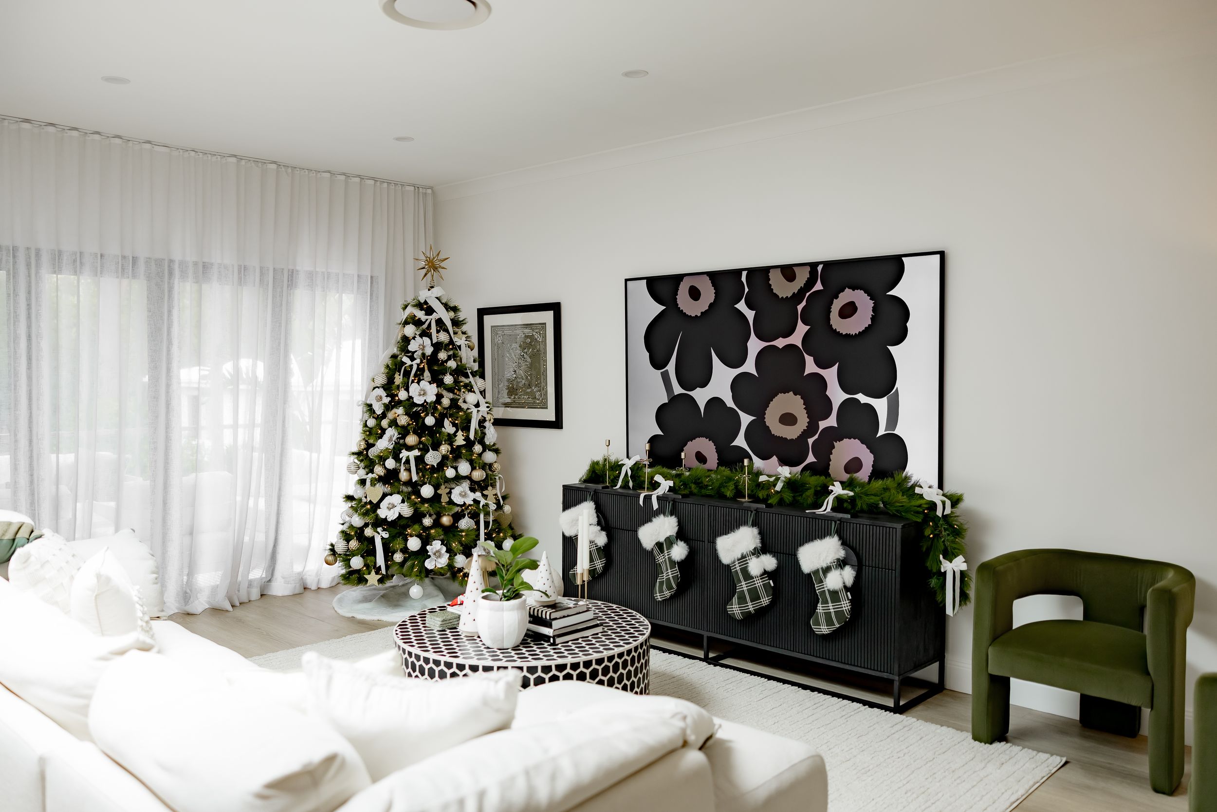 Modern white living room with decorated Christmas tree, black and white wall art, and olive green accent chair.