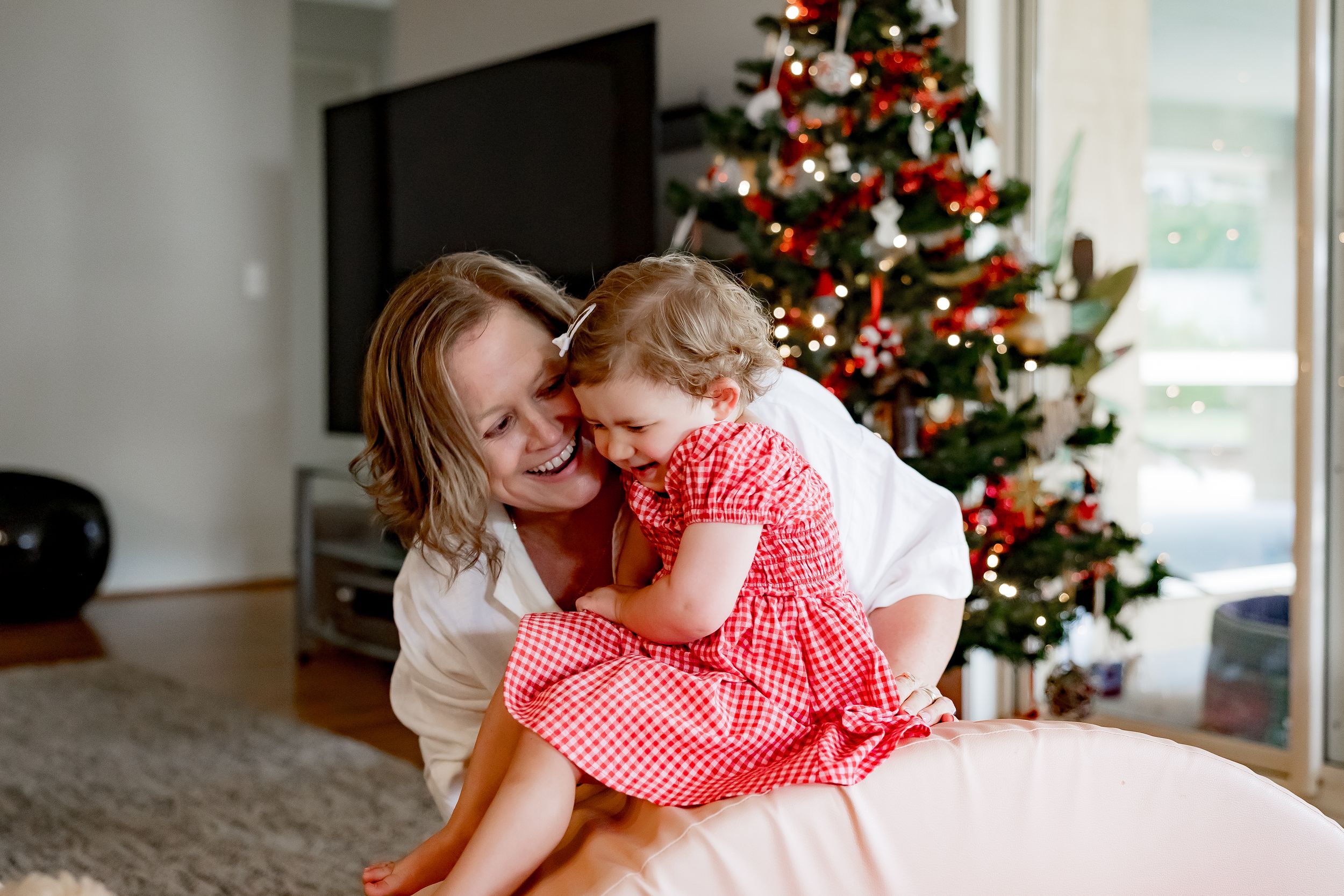 A loving moment between parent and child in front of a decorated Christmas tree during a holiday photoshoot.