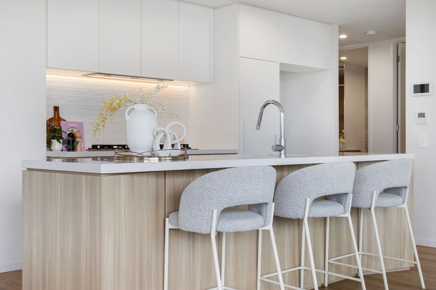 Modern white kitchen interior with minimalist design featuring bar stools and clean countertops.