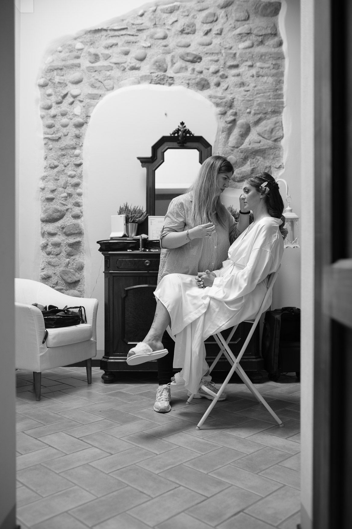 Black and white photo showing a vintage-style dressing room scene with an ornate mirror and stone wall interior.