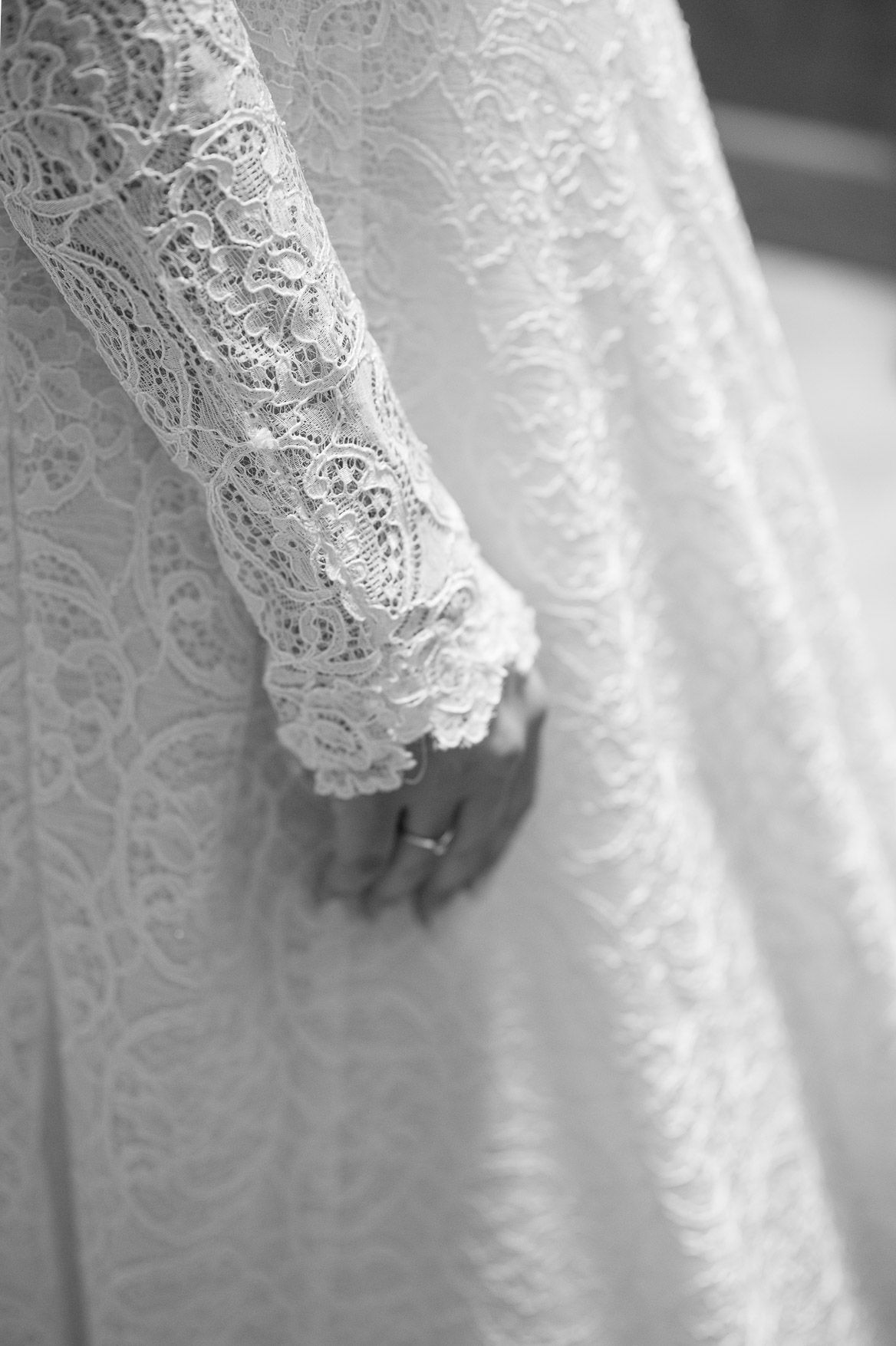 Close-up detail of delicate white lace sleeve on a wedding dress with a ring visible.