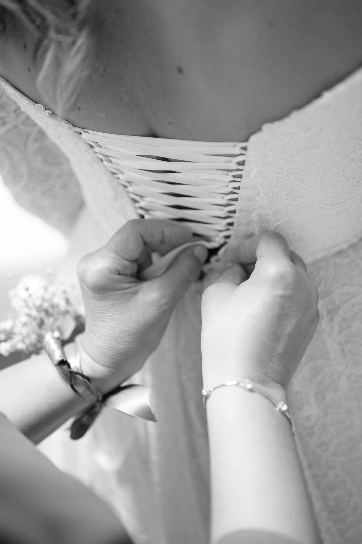 Close-up black and white details of a wedding dress being laced up from behind.