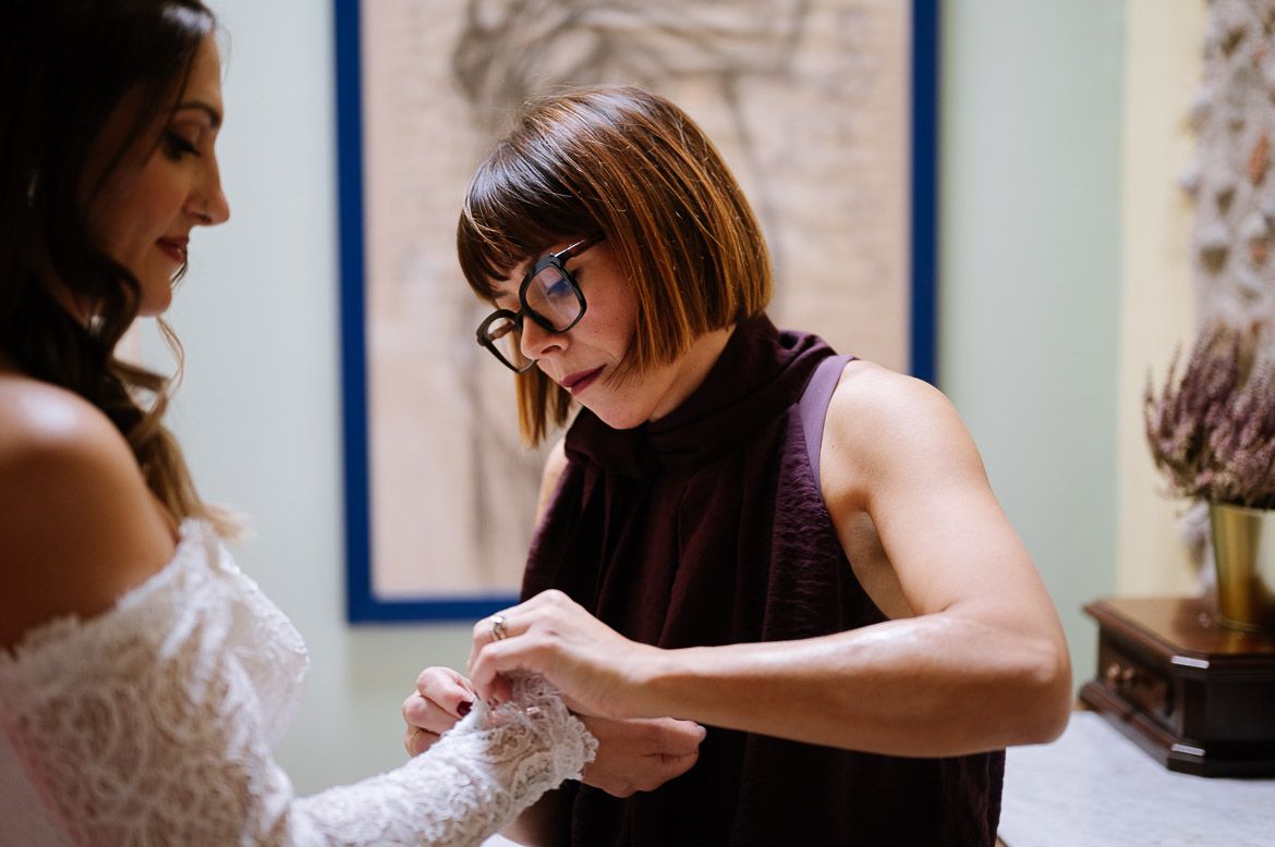 A dress fitting session shows careful attention to detail as adjustments are made to a white lace garment.