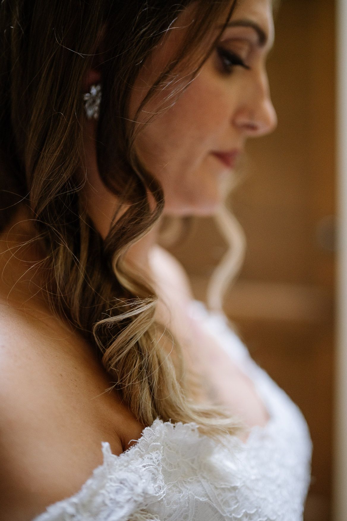 Side profile view of an elegant bridal look featuring soft waves and lace details.