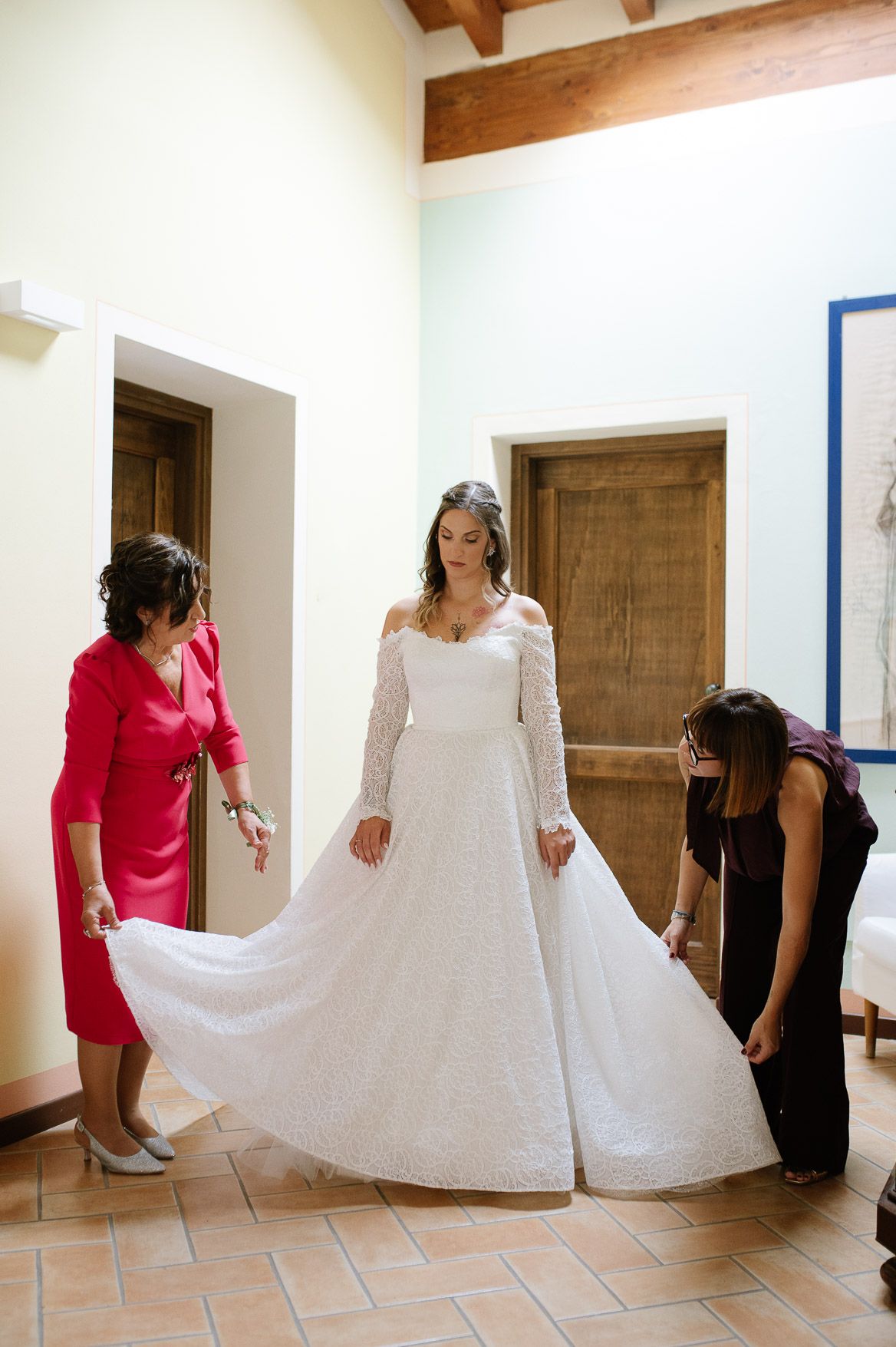 Series of shots showing people helping with a wedding dress train in a room with wooden beams and white walls.