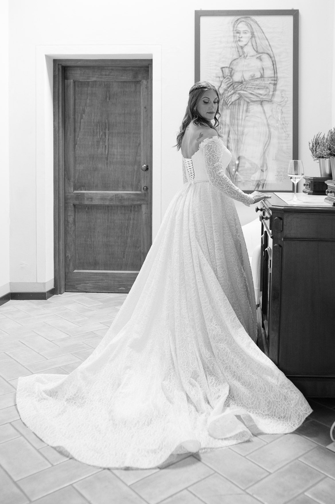 A flowing white wedding dress with intricate lace details and a long train displayed in a room.