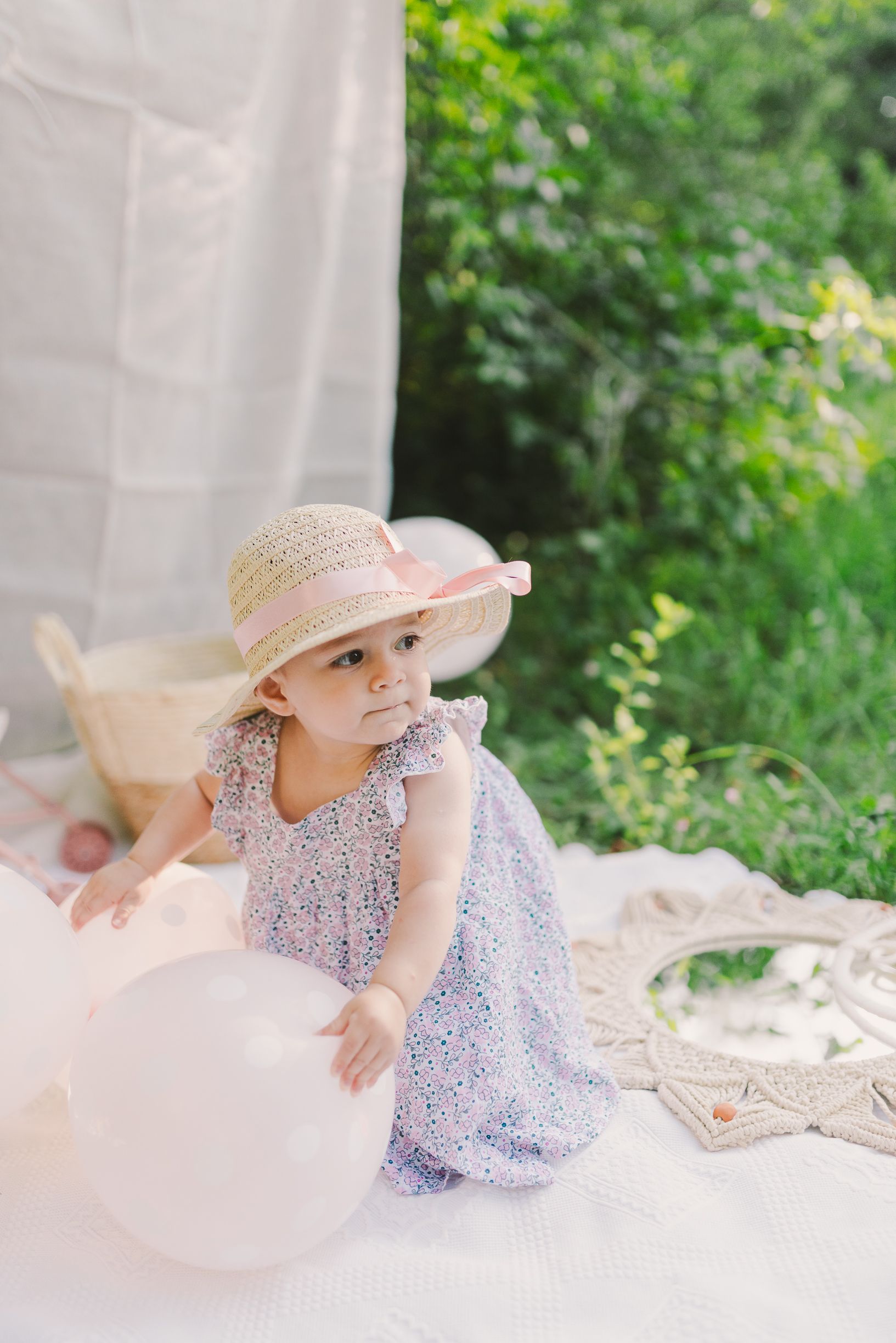 Child in a sun hat lying on a white blanket during an outdoor photoshoot.