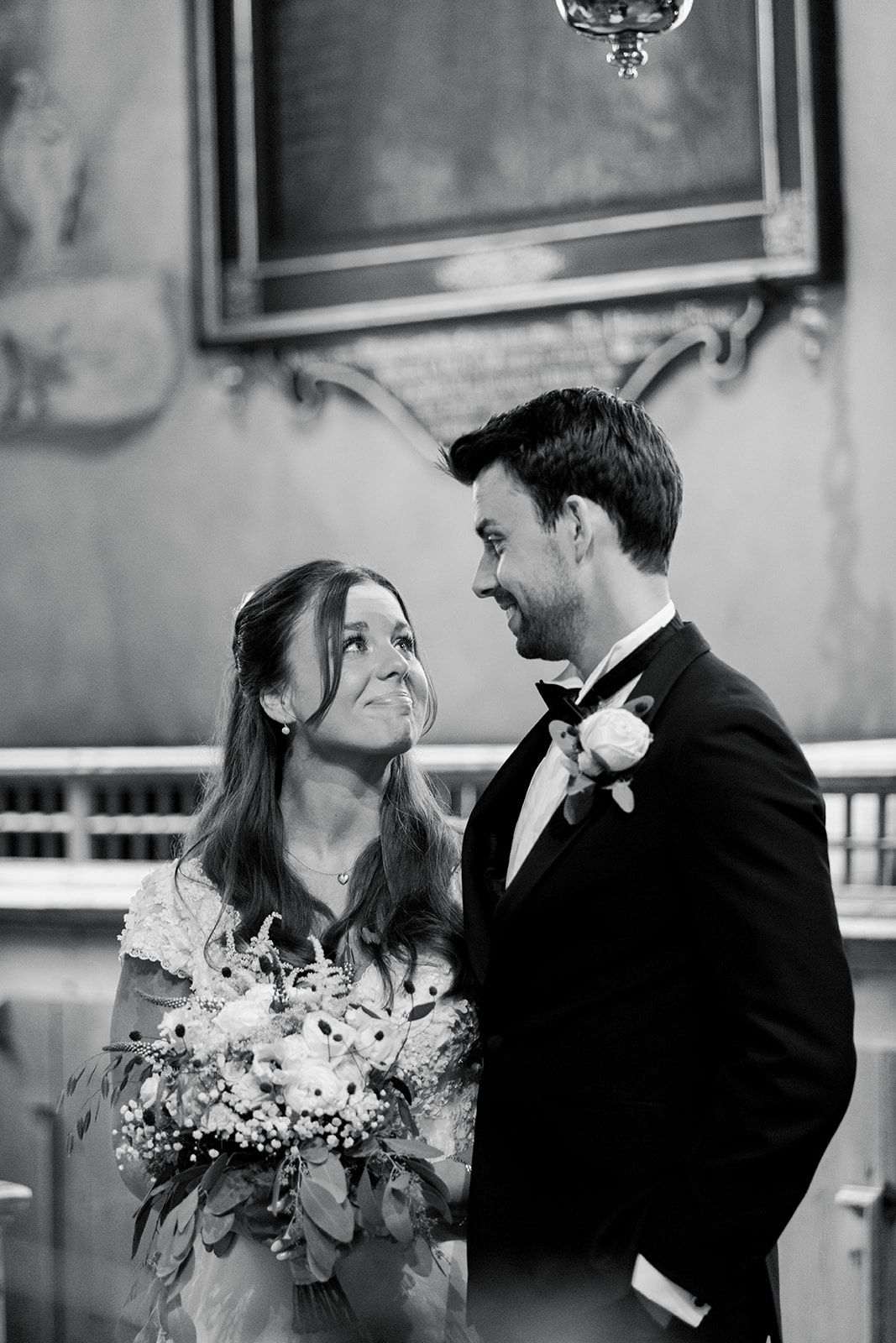 Black and white wedding photo of a couple sharing an intimate moment with the bride holding a floral bouquet.