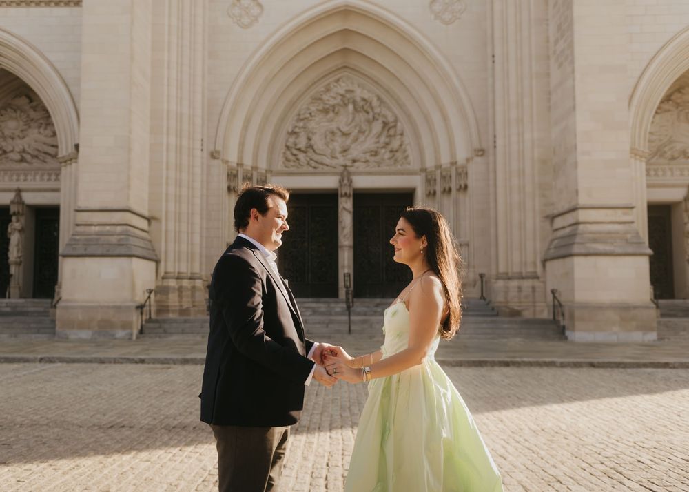 Elegant couple in formal attire dancing together in front of ornate stone cathedral architecture.