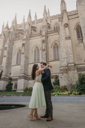 A romantic couple shares a tender moment in front of a grand gothic cathedral with ornate stone architecture.
