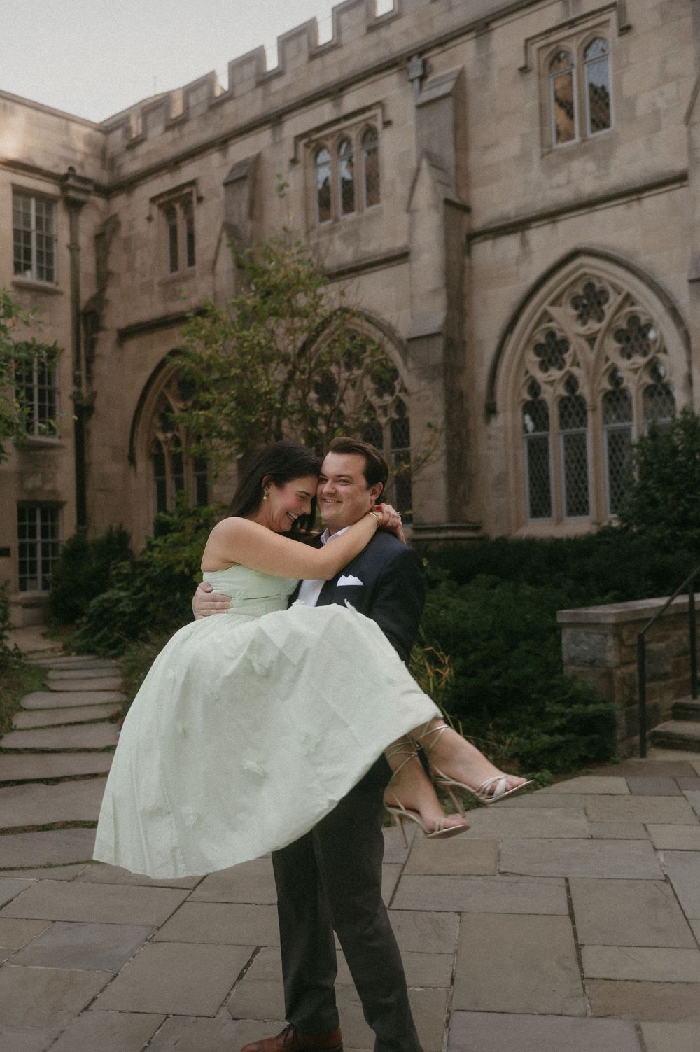 A couple shares a romantic dance pose in front of a Gothic stone building with arched windows and ornate architecture.