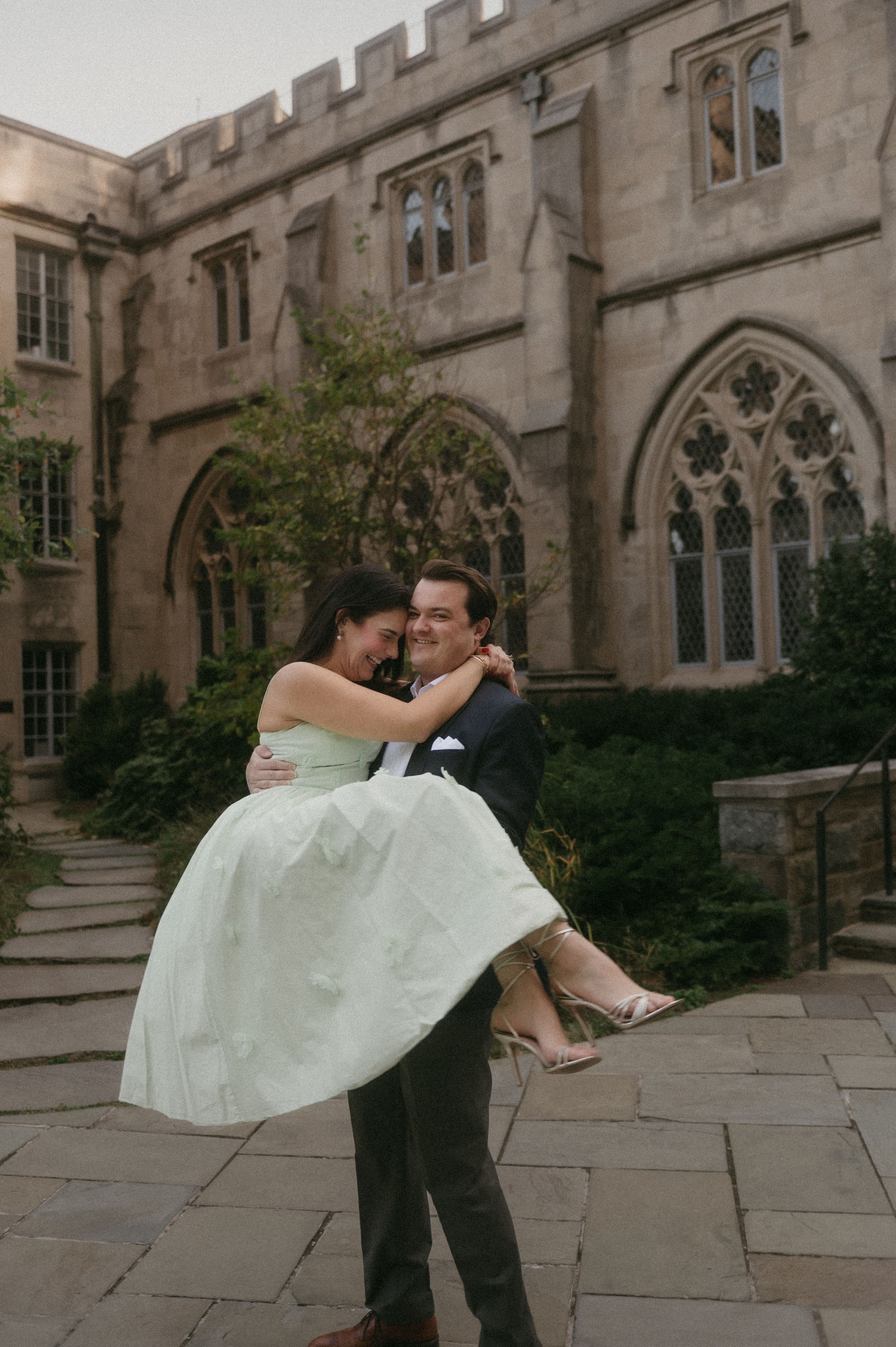 A couple shares a romantic dance pose in front of a Gothic stone building with arched windows and ornate architecture.