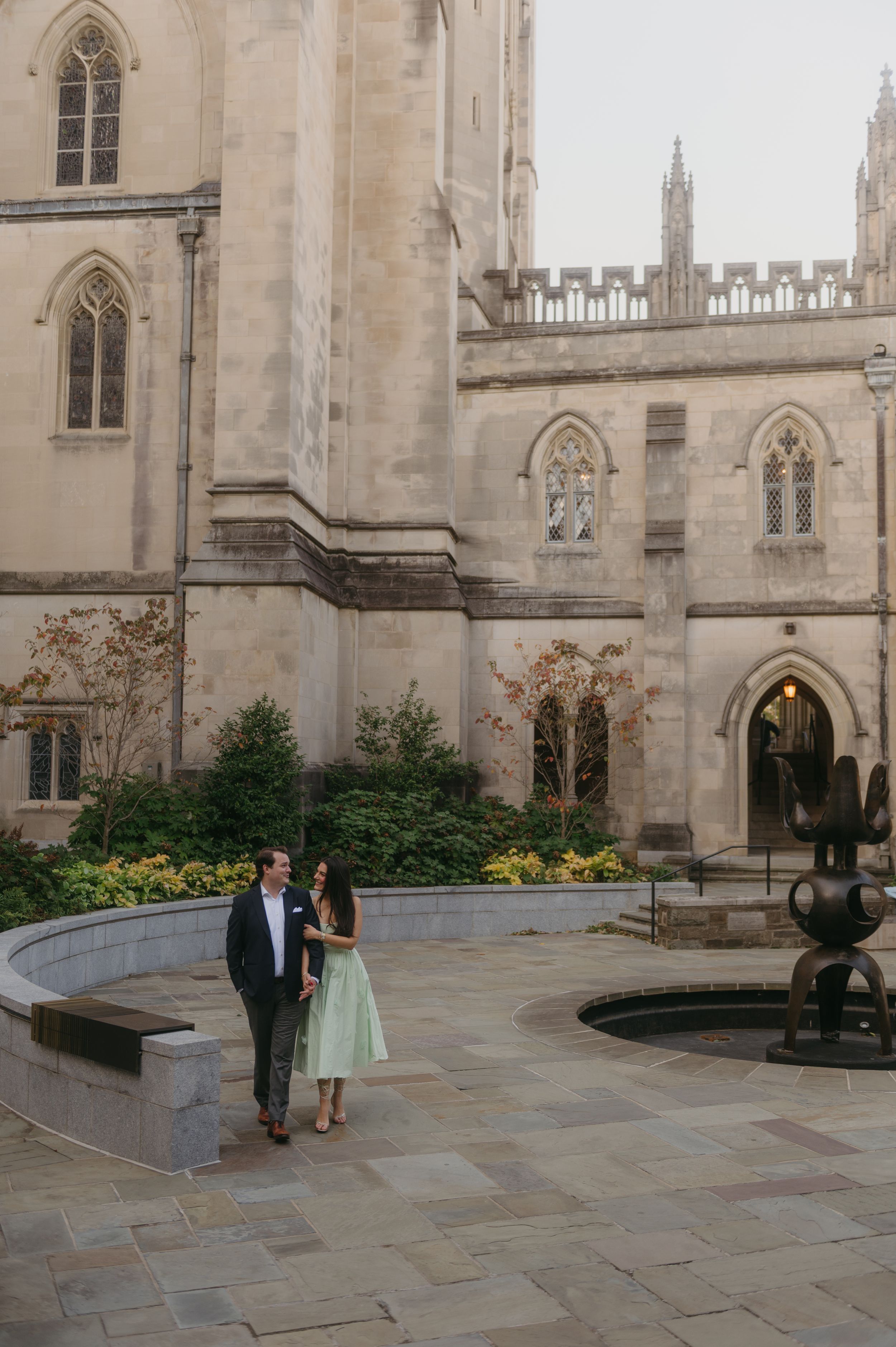 Couple sharing a romantic moment in front of a Gothic stone church courtyard with yellow flowers.