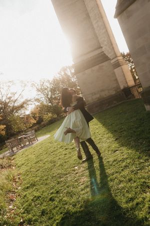 Person standing under concrete overpass on grassy slope during golden hour sunset casting long shadows.