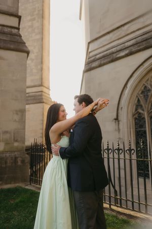 A couple in formal attire shares a playful moment dancing outside a stone church building.