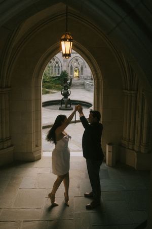 Two silhouettes dance together beneath a gothic stone archway with a glowing lantern overhead.