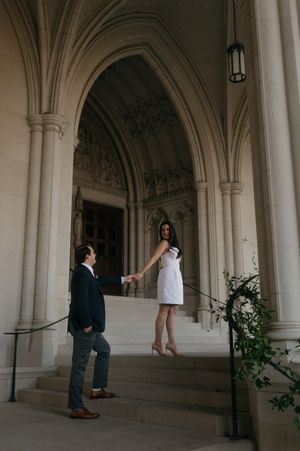 A bride and groom pose in an elegant stone archway corridor with white columns and decorative greenery.