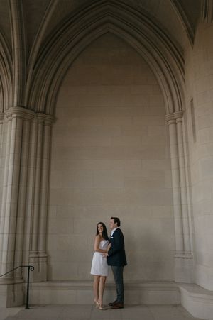 A romantic couple stands in an arched stone hallway of a historic building, creating an elegant architectural frame.