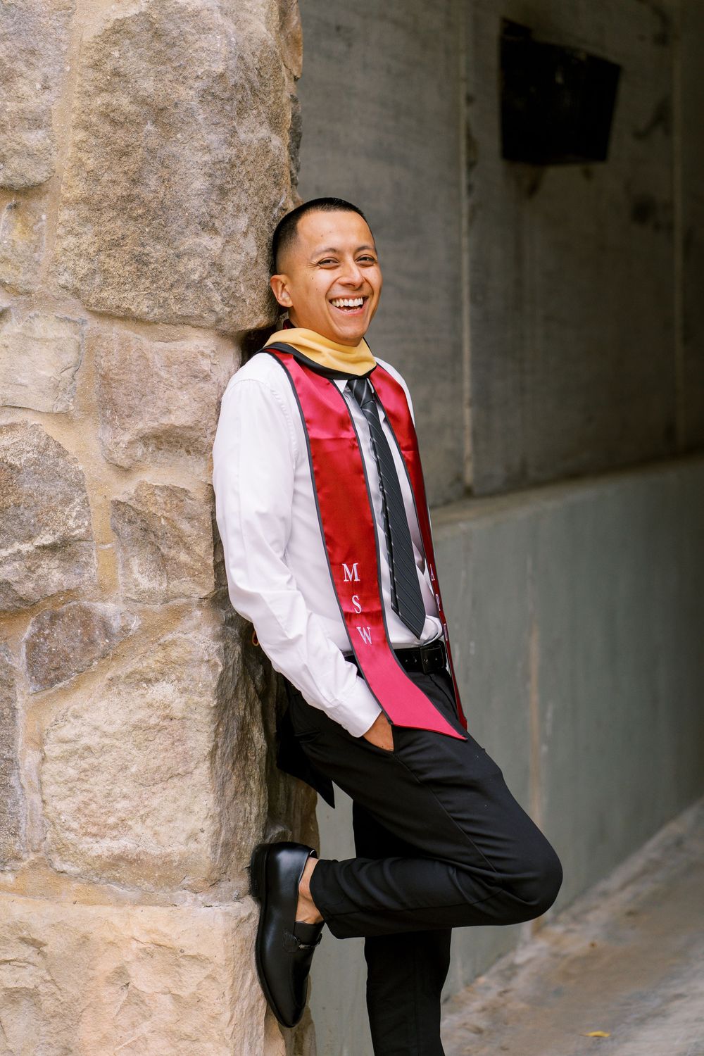 A person in formal attire with a red vest smiles while posing against a stone wall in three similar poses.