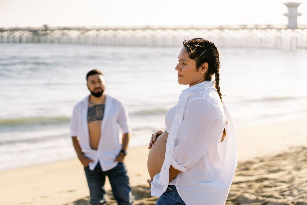 A couple sits together on a sandy beach during a romantic sunset photoshoot.