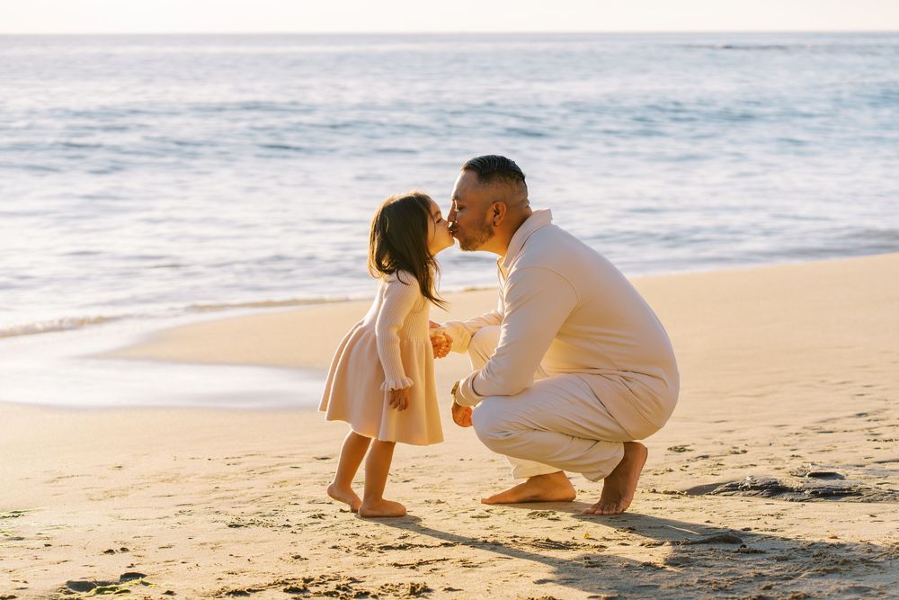 Two people sit together on a sandy beach at sunset sharing an intimate moment by the ocean waves.