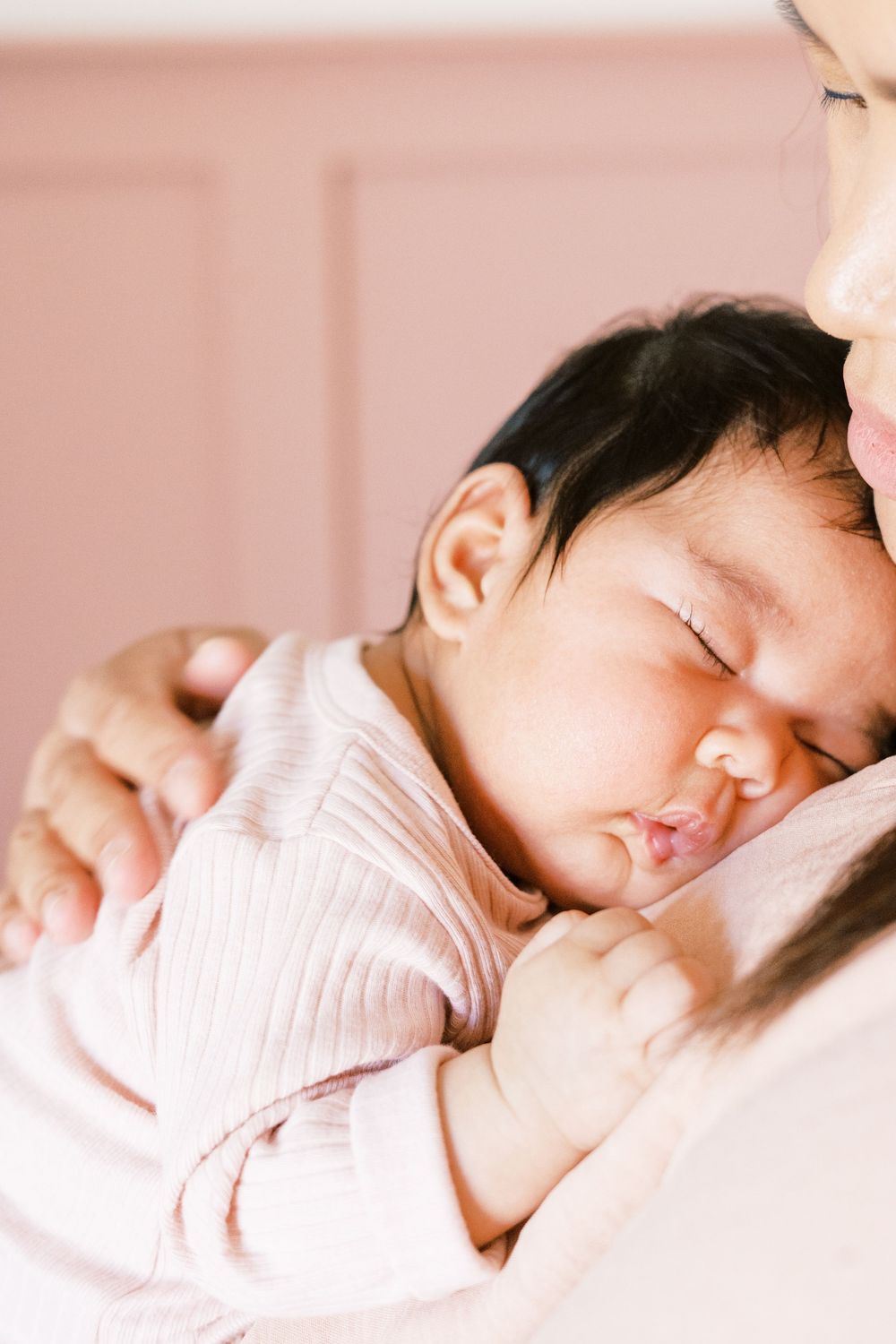 Peaceful sleeping baby in pink striped clothing rests against soft background in gentle lighting.