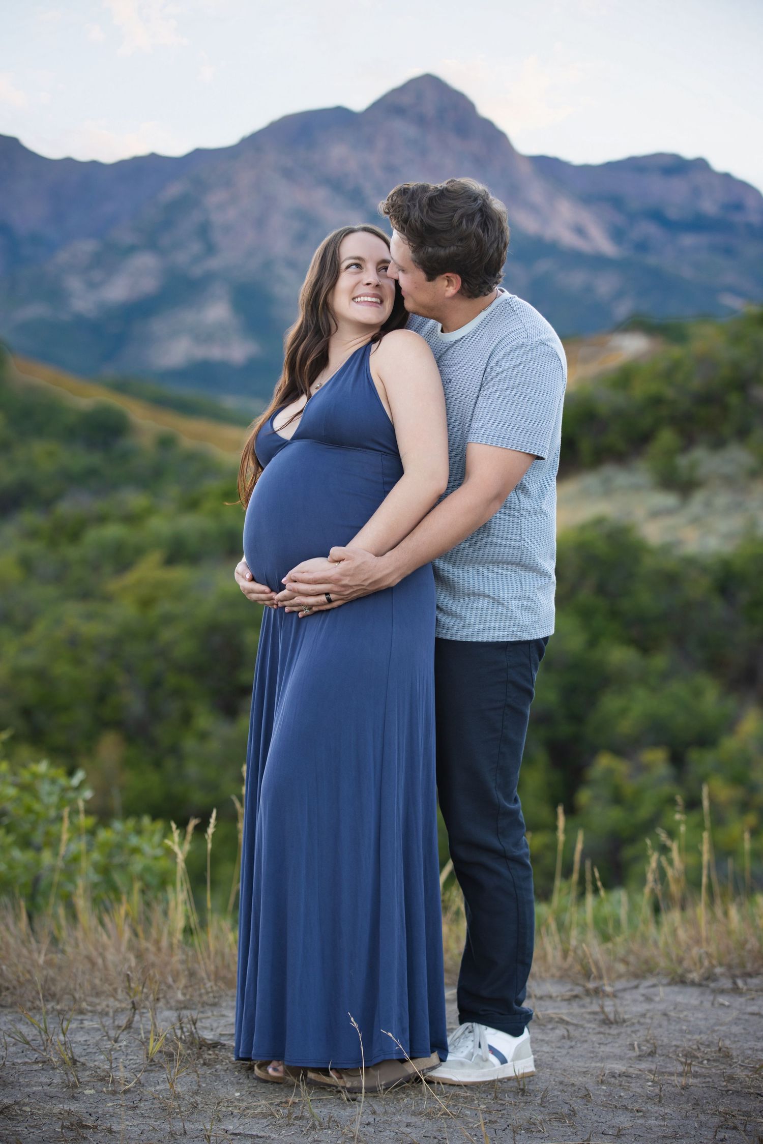 A pregnant lady in a black floral dress poses gracefully in the fall leaves in Ogden utah