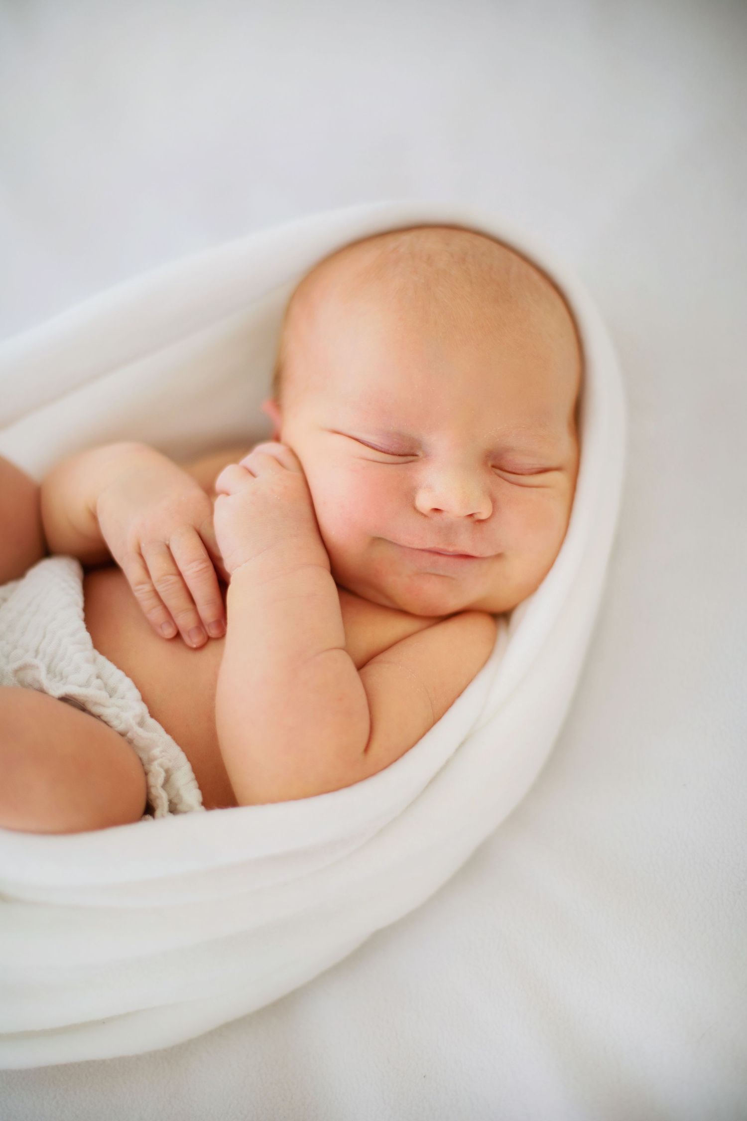 Sovande nyfödd baby insvept i mjuka vita filtar som visas i en serie fridfulla närbilder.