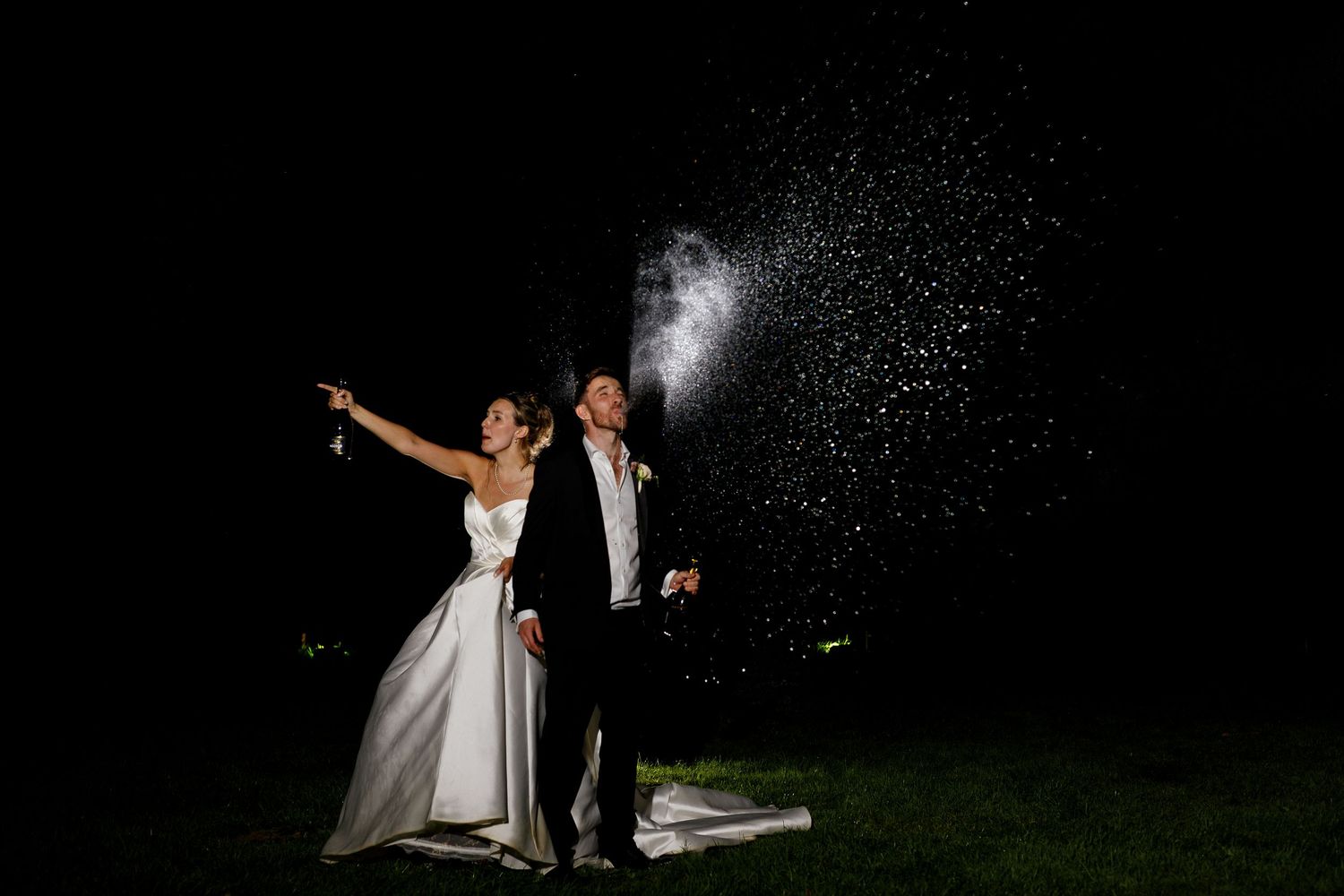 Wedding couple dances together under starry night sky while sparklers create magical light trails in the background.