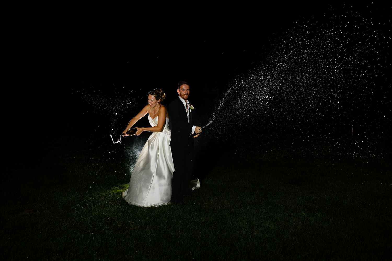 A wedding couple dances together under twinkling lights in a romantic outdoor nighttime setting.