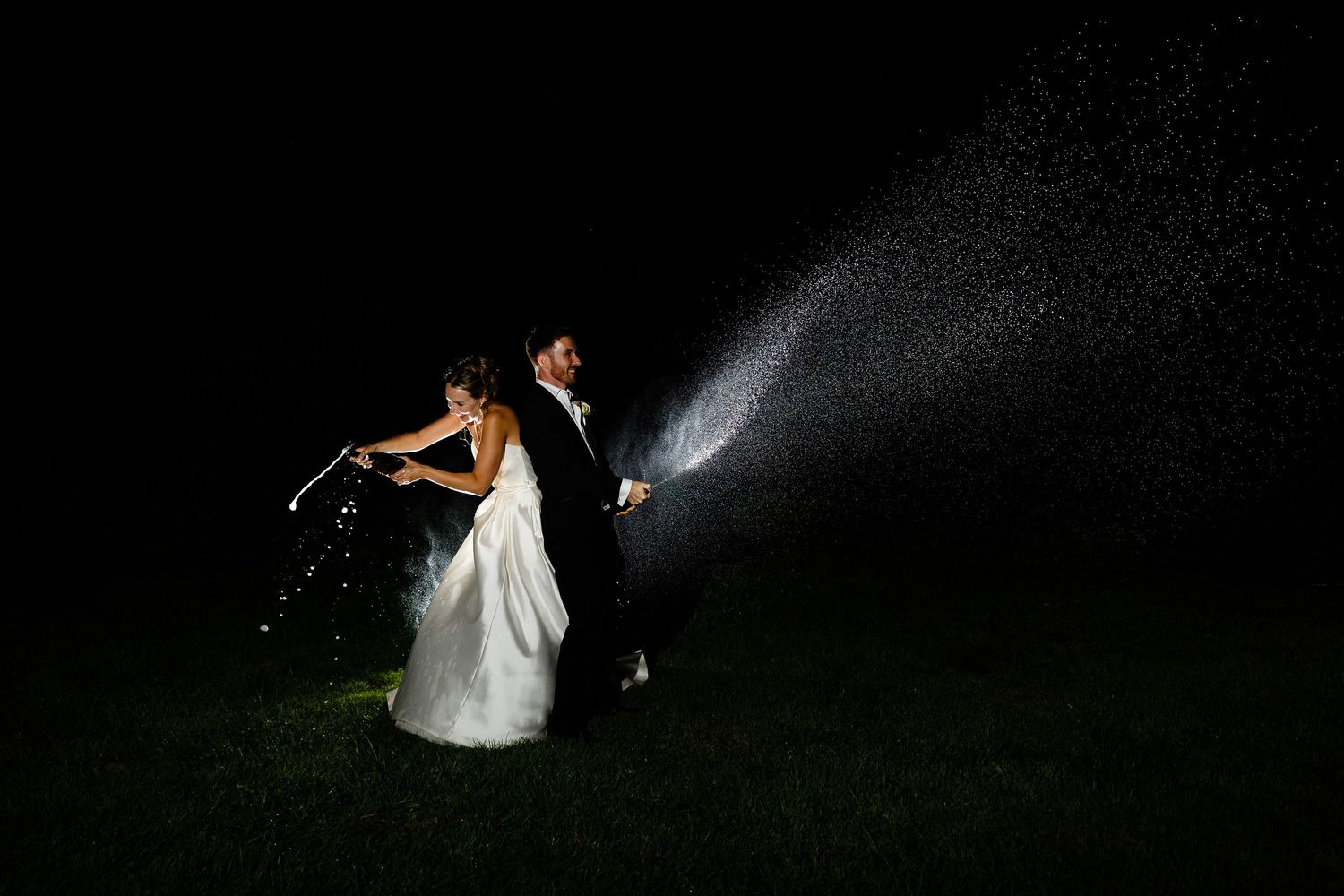 A couple in wedding attire dances together at night while sparklers create a magical light trail effect in the background.