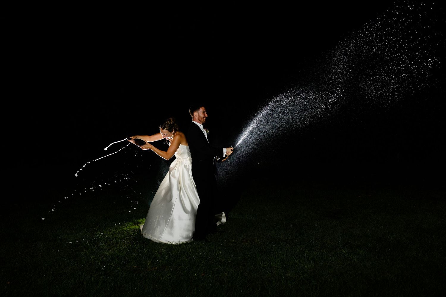 A couple in wedding attire dances and twirls together at night under dramatic lighting and sparklers.